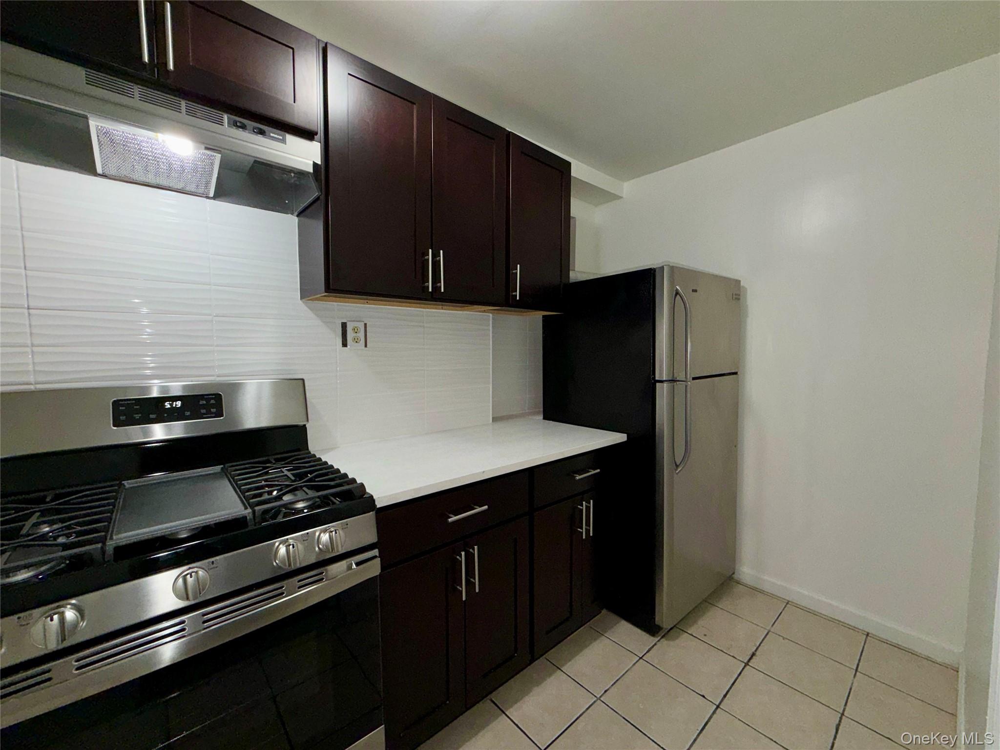 84-70 159th Street Queens, NY 11432 - Photo 26 of 50 Kitchen featuring stainless steel appliances, decorative backsplash, range hood, dark brown cabinets, and light tile patterned flooring