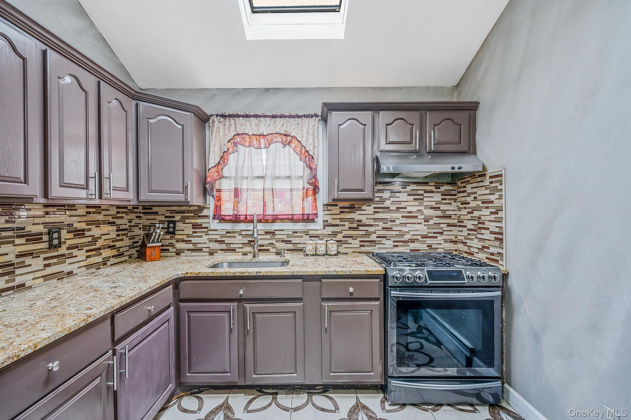 84-70 159th Street Queens, NY 11432 - Photo 8 of 50 Kitchen featuring gas range, a skylight, light stone counters, under cabinet range hood, and lofted ceiling