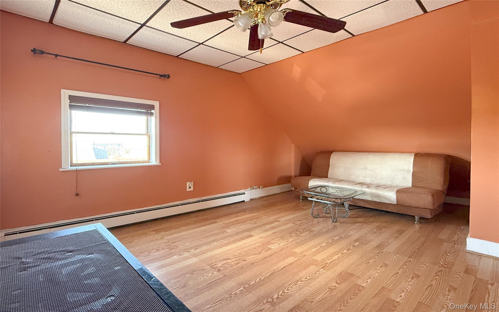 134-37 58th Road Queens, NY 11355 - Photo 18 of 24 Unfurnished room featuring a baseboard radiator, light wood finished floors, a paneled ceiling, a ceiling fan, and vaulted ceiling