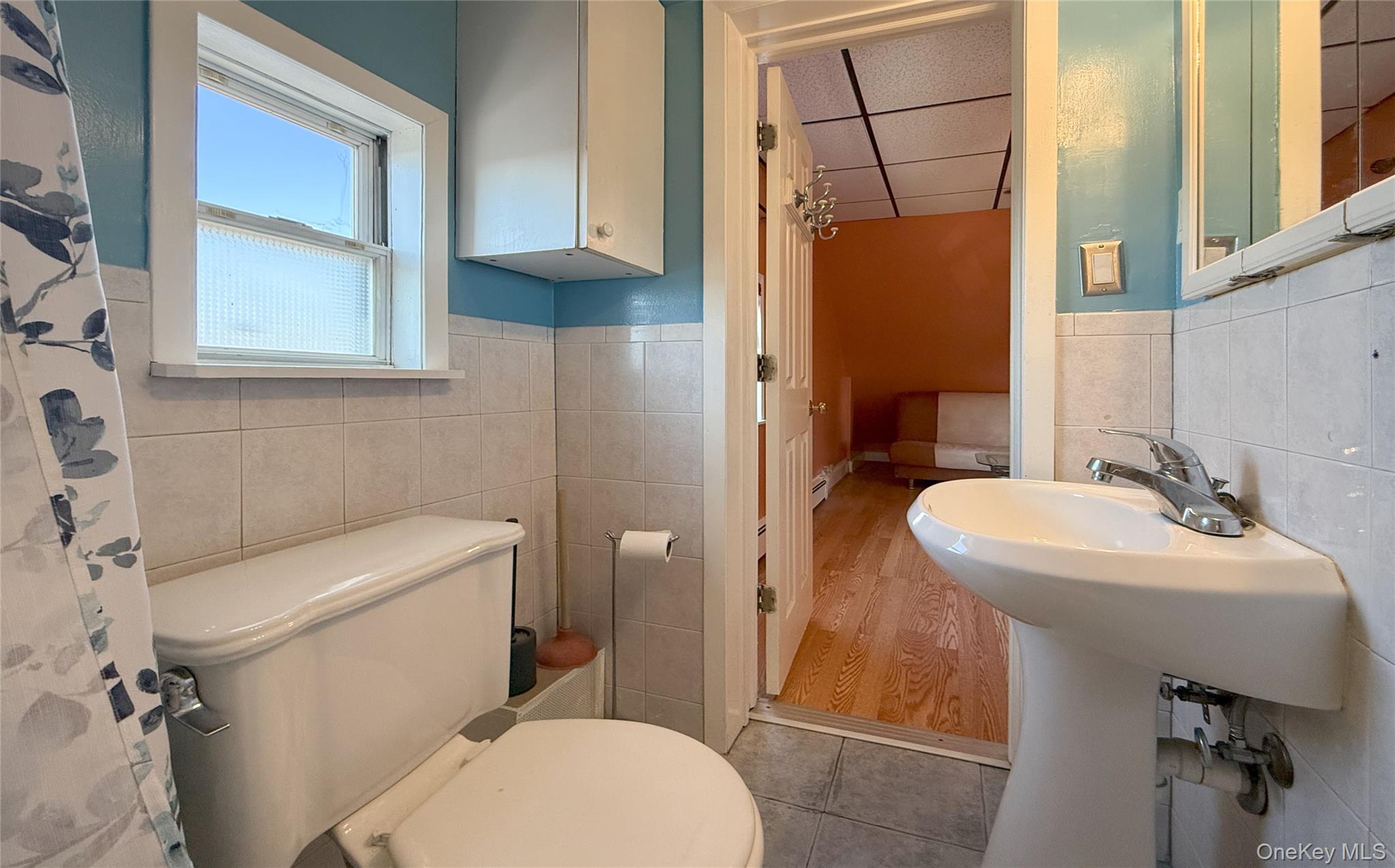 134-37 58th Road Queens, NY 11355 - Photo 23 of 24 Full bath with tile walls, a wainscoted wall, a paneled ceiling, light tile patterned floors, and a shower with curtain