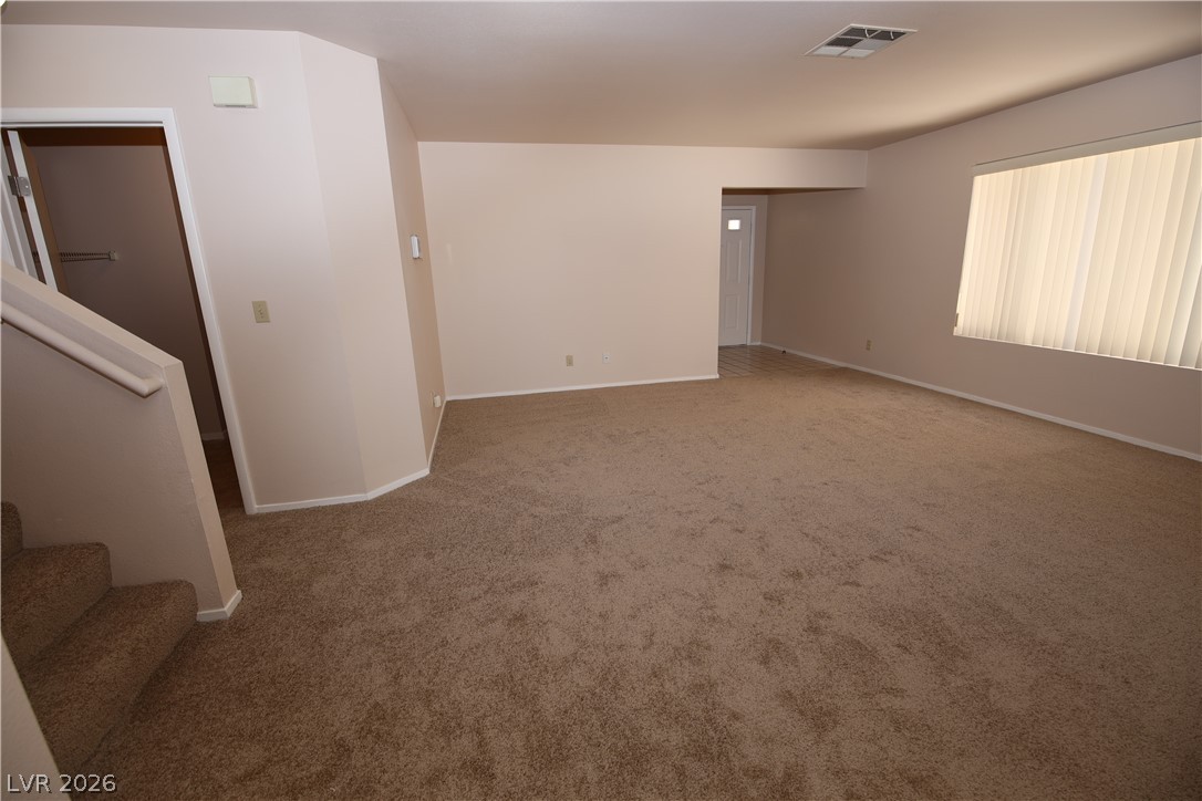 8220 Maplestar Road Las Vegas, NV 89128 - Photo 7 of 29 A spacious living area with warm-toned carpet and vertical blinds offers a comfortable setting.