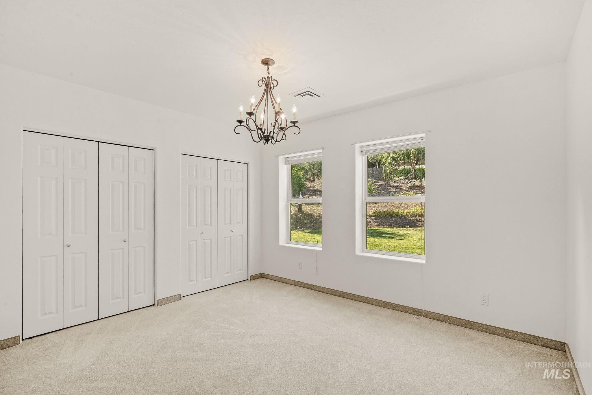 1091 Cedar Ridge Road Kendrick, ID 83537 - Photo 37 of 48 Room featuring a decorative chandelier, dual windows, two sets of bi-fold closet doors, and carpet flooring with a tile baseboard