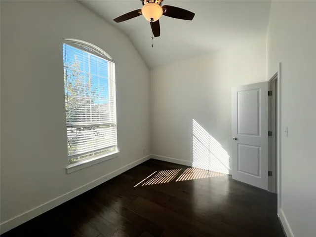 an empty room with wooden floor chandelier fan and windows