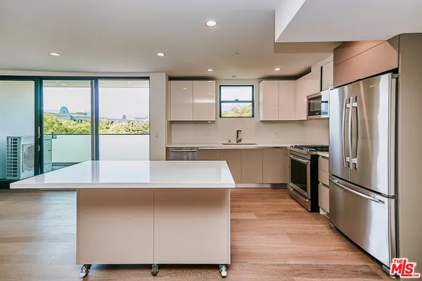 a kitchen with kitchen island a counter top space a refrigerator wooden floor and a large window