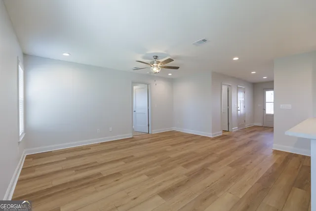 a view of an empty room with wooden floor and a ceiling fan