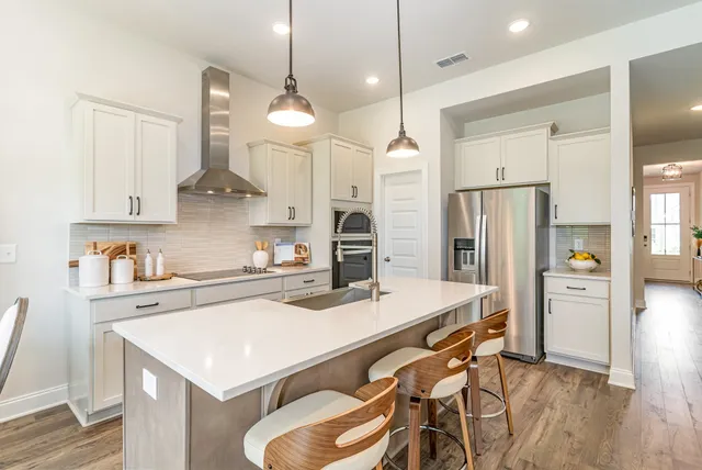 a kitchen with stainless steel appliances a stove a sink a refrigerator and chairs