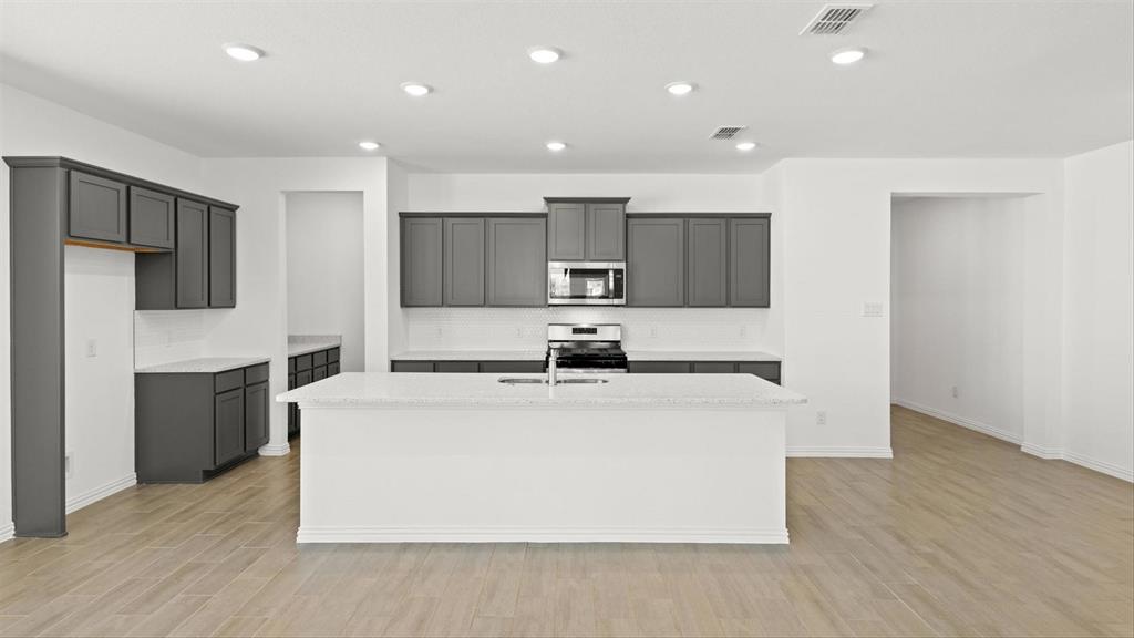 2747 Teton Street Corinth, TX 76210 - Photo 8 of 22 a large kitchen with stainless steel appliances granite countertop a stove a sink a refrigerator and white cabinets with wooden floor