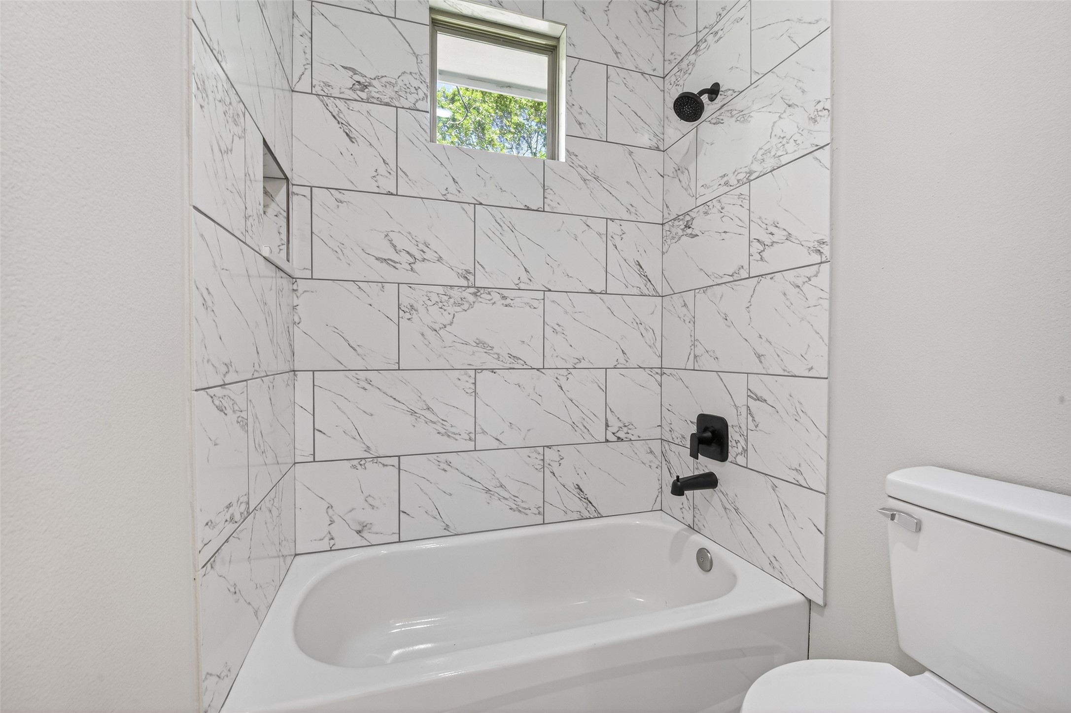 4930 Wunder Way Houston, TX 77069 - Photo 16 of 23 This bathroom features a sleek design with a white bathtub and black fixtures. The walls are adorned with elegant white tiles with gray veining, and a small window provides natural light.
