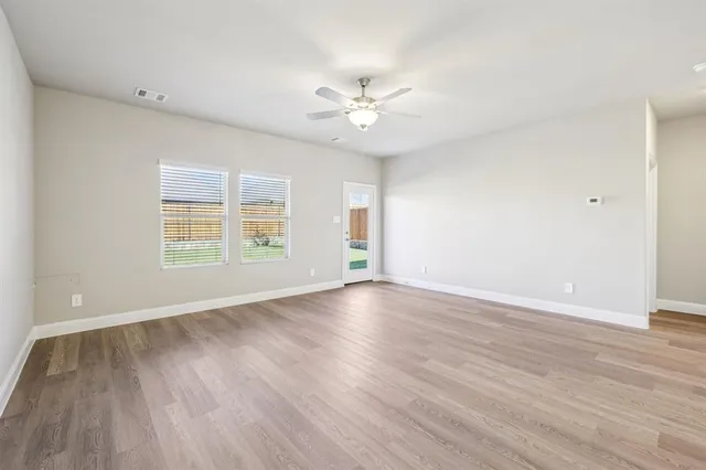 an empty room with wooden floor window and ceiling fan