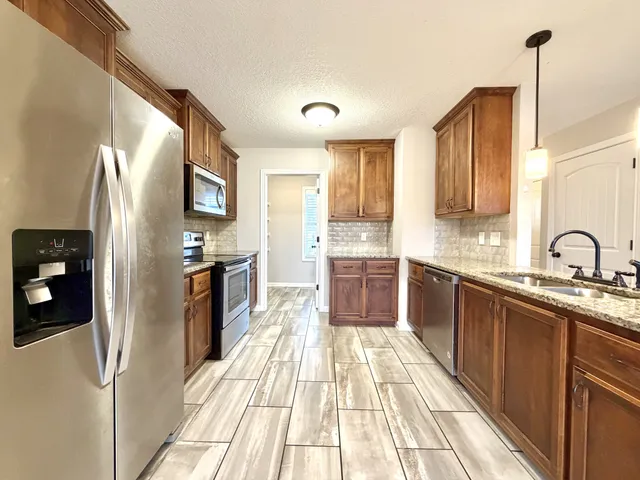 a kitchen with stainless steel appliances granite countertop a refrigerator a sink dishwasher a stove and white countertops with wooden floor