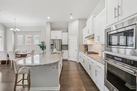 a large kitchen with stainless steel appliances kitchen island granite countertop a stove a sink dishwasher and a refrigerator with wooden floor