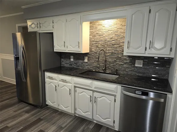 a kitchen with stainless steel appliances granite countertop a refrigerator a sink and white cabinets with wooden floor