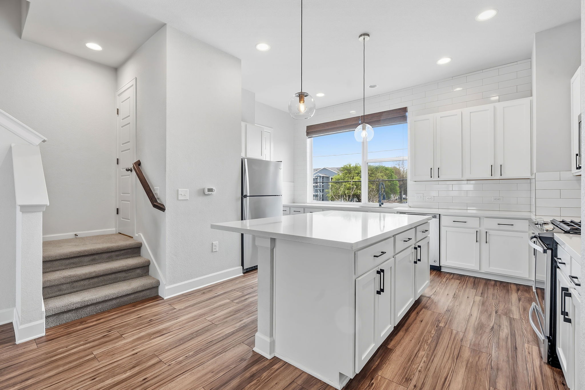4409 Festival Path, Unit 26 Austin, TX 78741 - Photo 3 of 24 Kitchen with a kitchen island, stainless steel appliances, pendant lighting, backsplash, and white cabinets