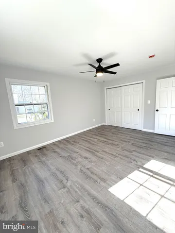 an empty room with wooden floor ceiling fan and windows
