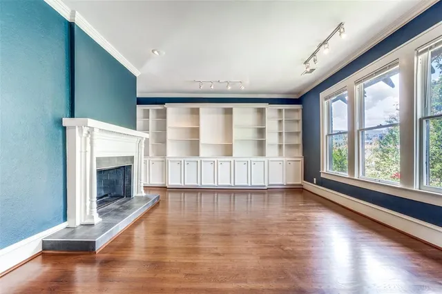 a view of an empty room with wooden floor fireplace and a window