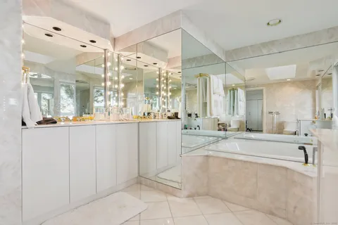 a large white bathroom with a large mirror vanity and a bath tub