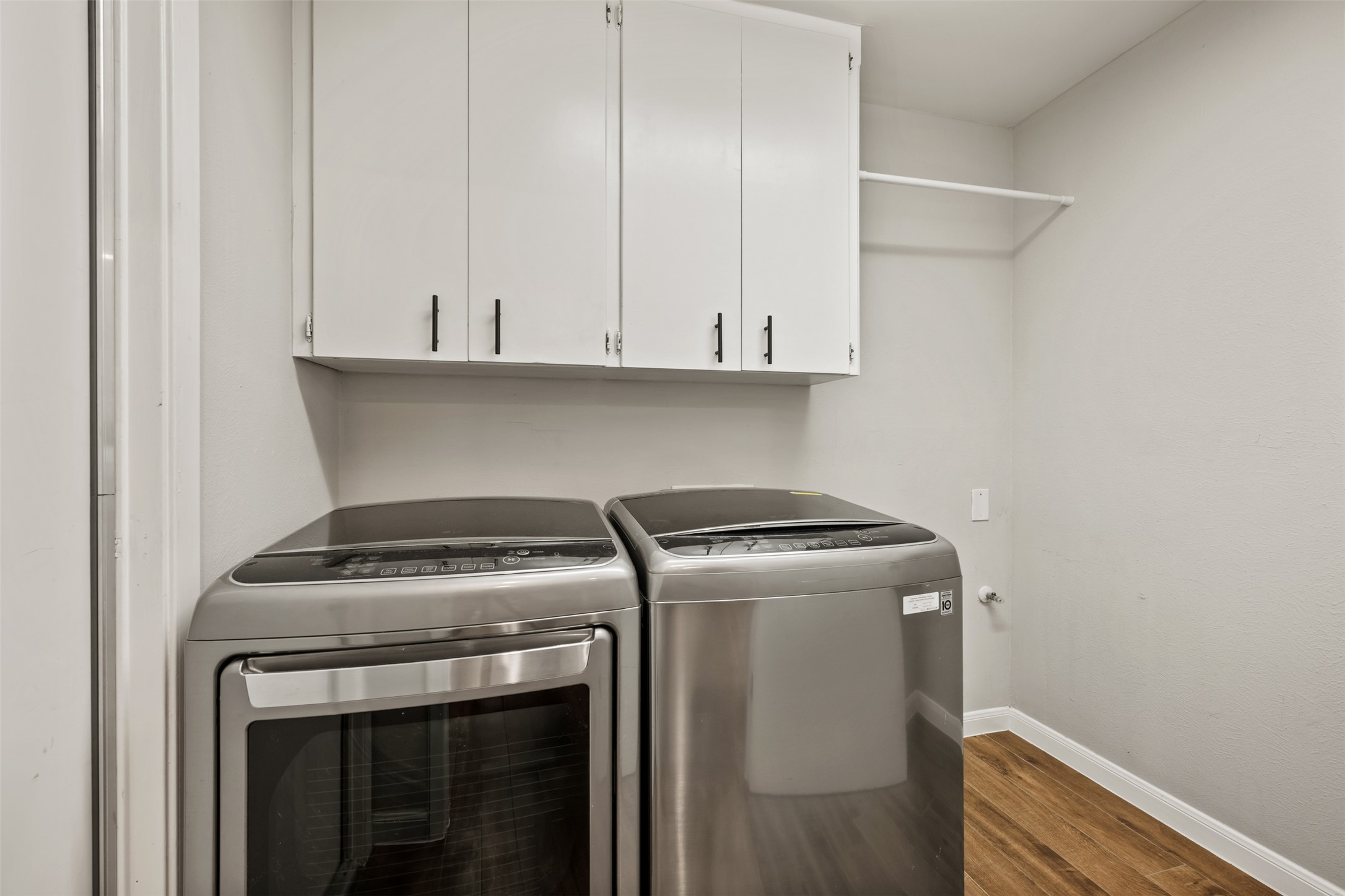 1600 Pin Oak Lane Round Rock, TX 78681 - Photo 33 of 40 Dedicated laundry space featuring wood-finish flooring, white wall cabinetry with dark hardware, and a wall-mounted drying rod