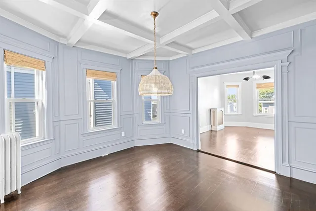 an empty room with wooden floor chandelier and windows
