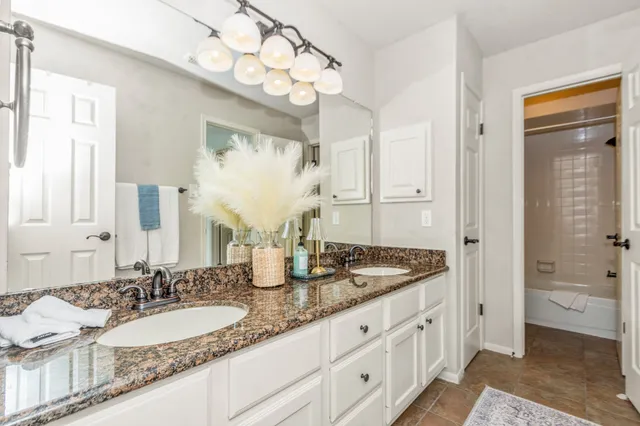 a bathroom with a granite countertop double vanity sink a mirror and a shower