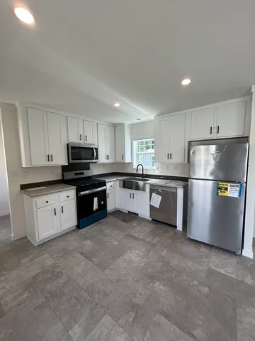 a kitchen with stainless steel appliances granite countertop a refrigerator a stove a sink and white cabinets