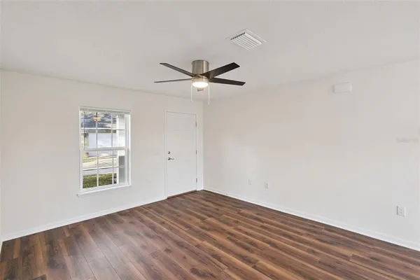 an empty room with wooden floor ceiling fan and windows