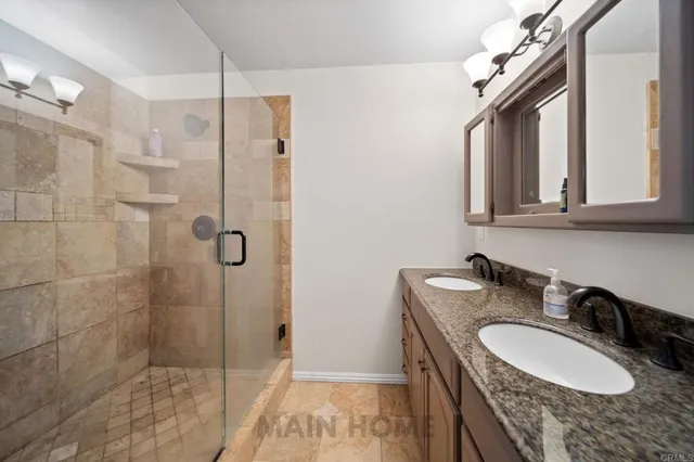 a bathroom with a granite countertop double vanity sink a mirror and shower
