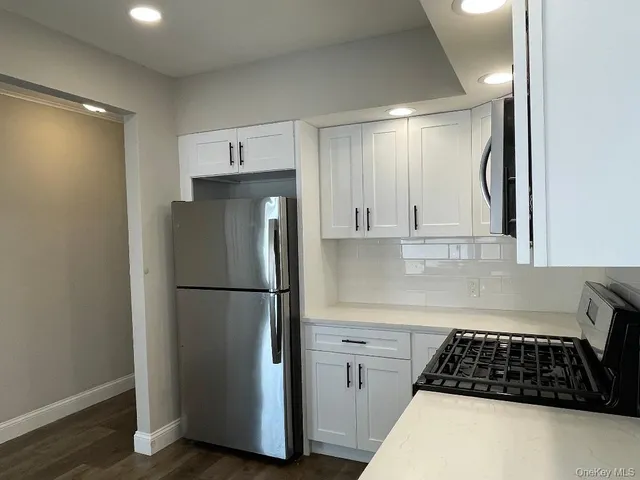 a kitchen with a refrigerator a stove and white cabinets with wooden floor