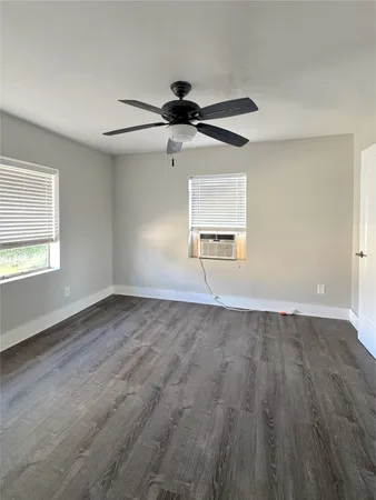 an empty room with wooden floor ceiling fan and windows