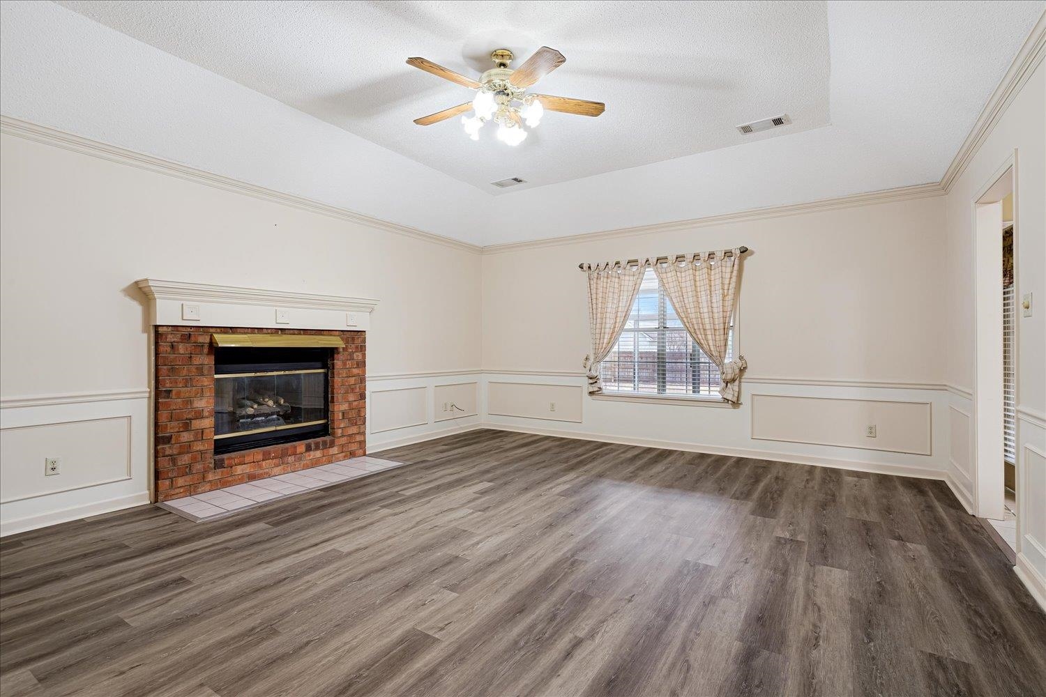 489 Autumn Trail Cove Collierville, TN 38017 - Photo 9 of 30 an empty room with wooden floor a ceiling fan a fireplace and windows