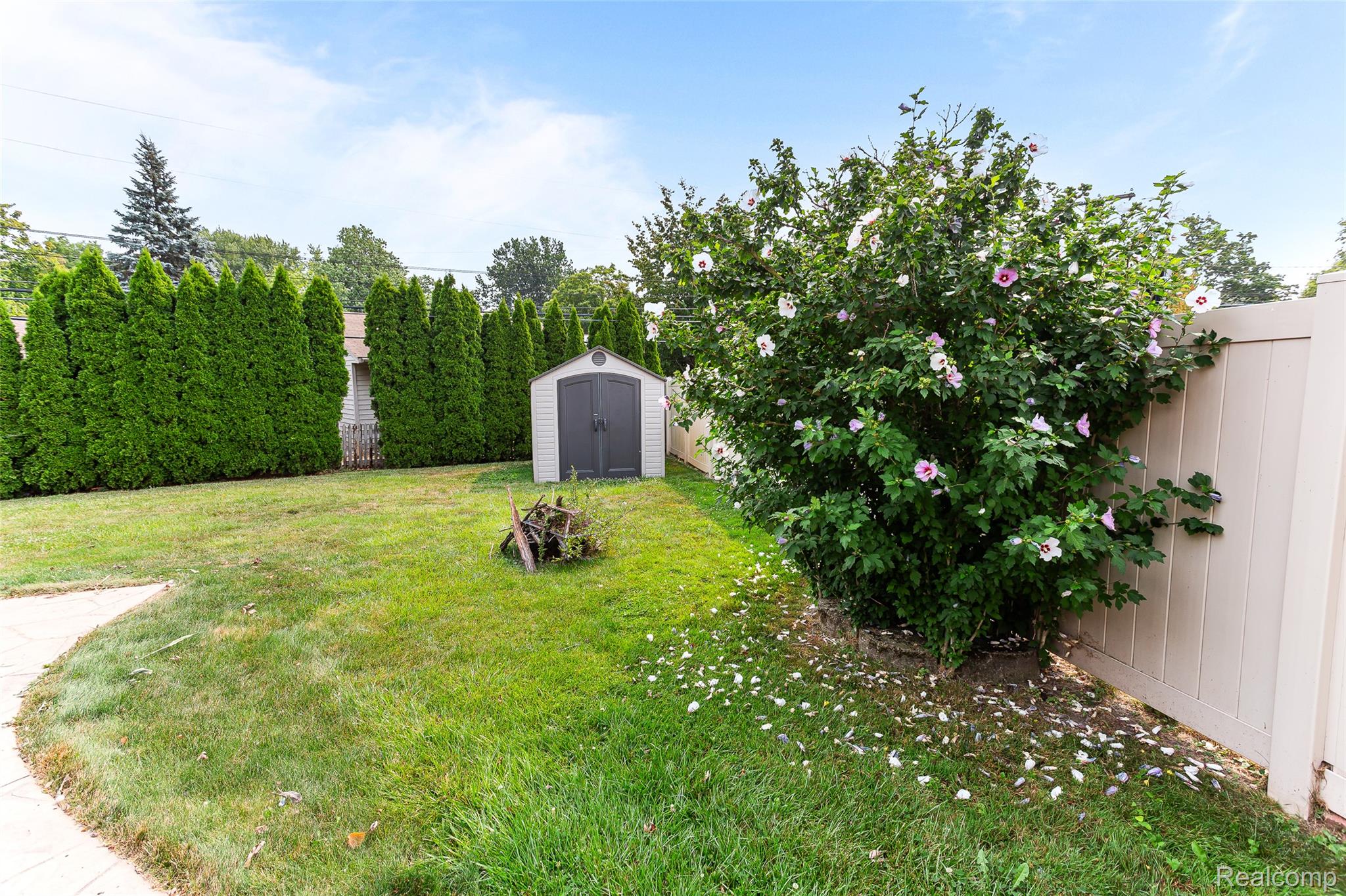 2345 Middlefield Road Trenton, MI 48183 - Photo 42 of 42 Expansive backyard featuring a lush lawn, privacy fencing, mature shrubbery with pink blooms, a storage shed, and a paved pathway