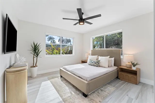 a white bed sitting in a bedroom next to a window with a flat screen tv