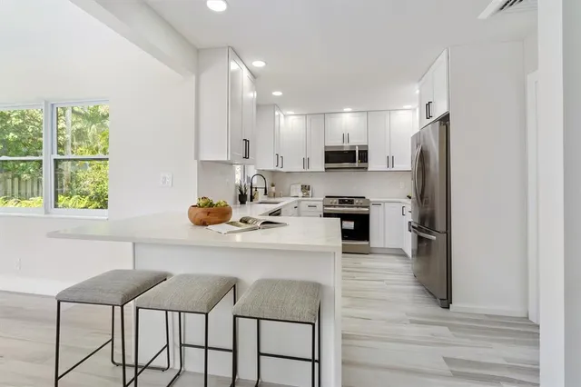 a kitchen with stainless steel appliances granite countertop a stove a sink a refrigerator and white cabinets with wooden floor