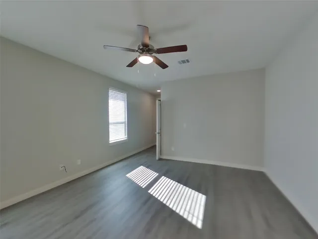 an empty room with wooden floor fan and windows