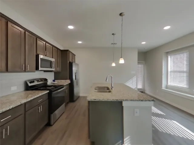 a kitchen with stainless steel appliances granite countertop a sink a stove a refrigerator cabinets and wooden floor