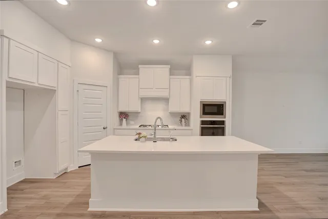a large white kitchen with kitchen island stainless steel appliances a sink and cabinets
