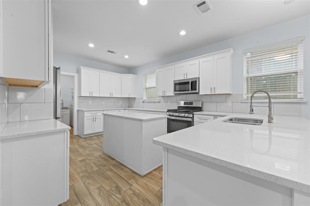 3807 Winding Road Arlington, TX 76016 - Photo 4 of 23 Modern kitchen featuring white shaker cabinetry, light-toned countertops, a central island, stainless steel appliances, and wood-finish flooring
