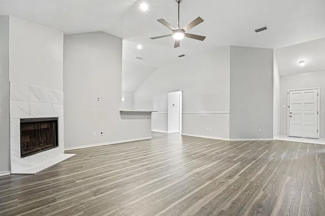 an empty room with wooden floor a ceiling fan a fireplace and windows