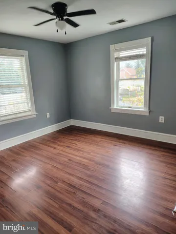 an empty room with wooden floor a ceiling fan and windows