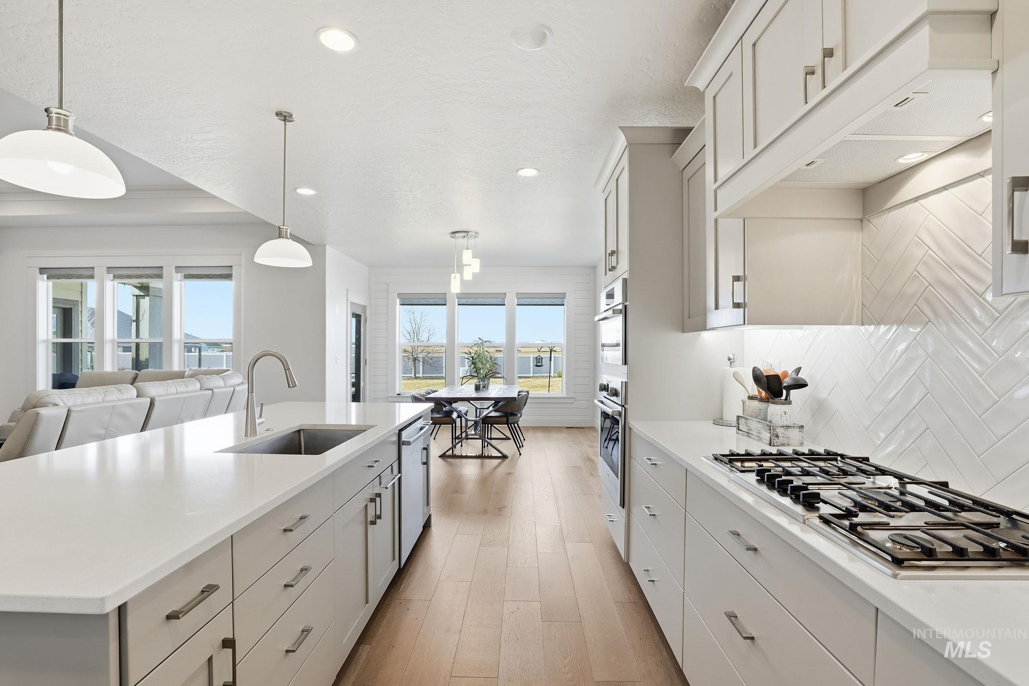 2301 Nordic Avenue Middleton, ID 83644 - Photo 14 of 50 Kitchen featuring a center island with sink, white cabinets, stainless steel appliances, decorative light fixtures, and light wood finished floors