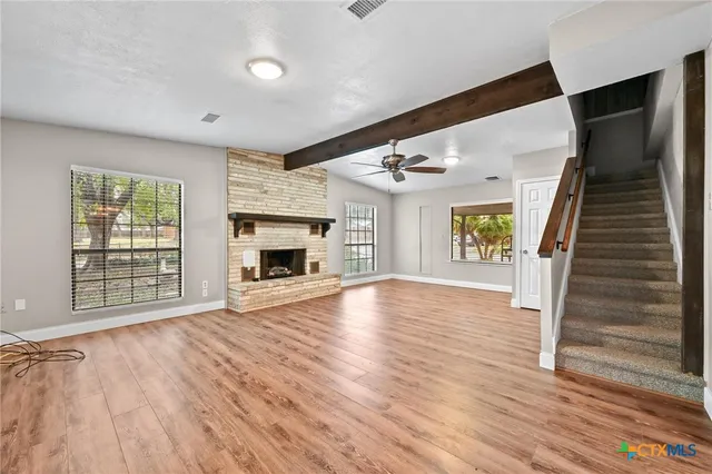 a view of an empty room with wooden floor fireplace and a window