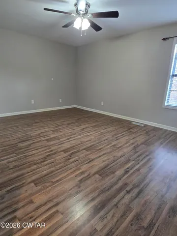 an empty room with wooden floor chandelier fan and windows