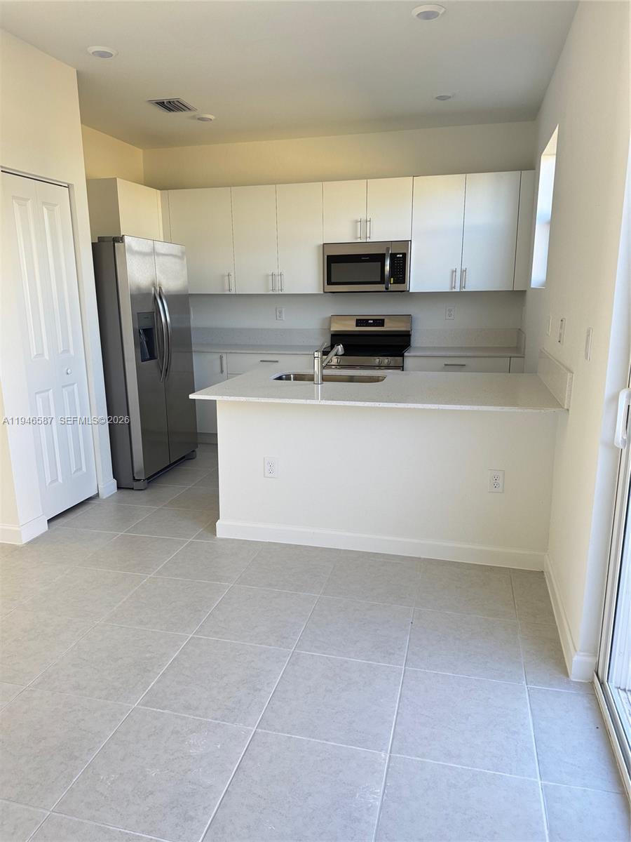 17953 Southwest 359th Street, Unit 17953 Homestead, FL 33034 - Photo 6 of 32 a kitchen with a refrigerator a stove a microwave and cabinets