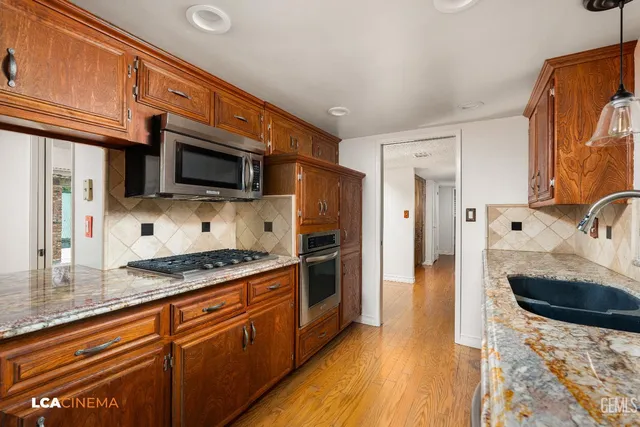 a kitchen with stainless steel appliances granite countertop a sink a stove top oven a refrigerator cabinets and wooden floor