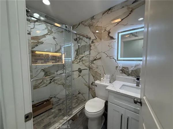 a bathroom with a granite countertop sink a toilet a mirror and shower