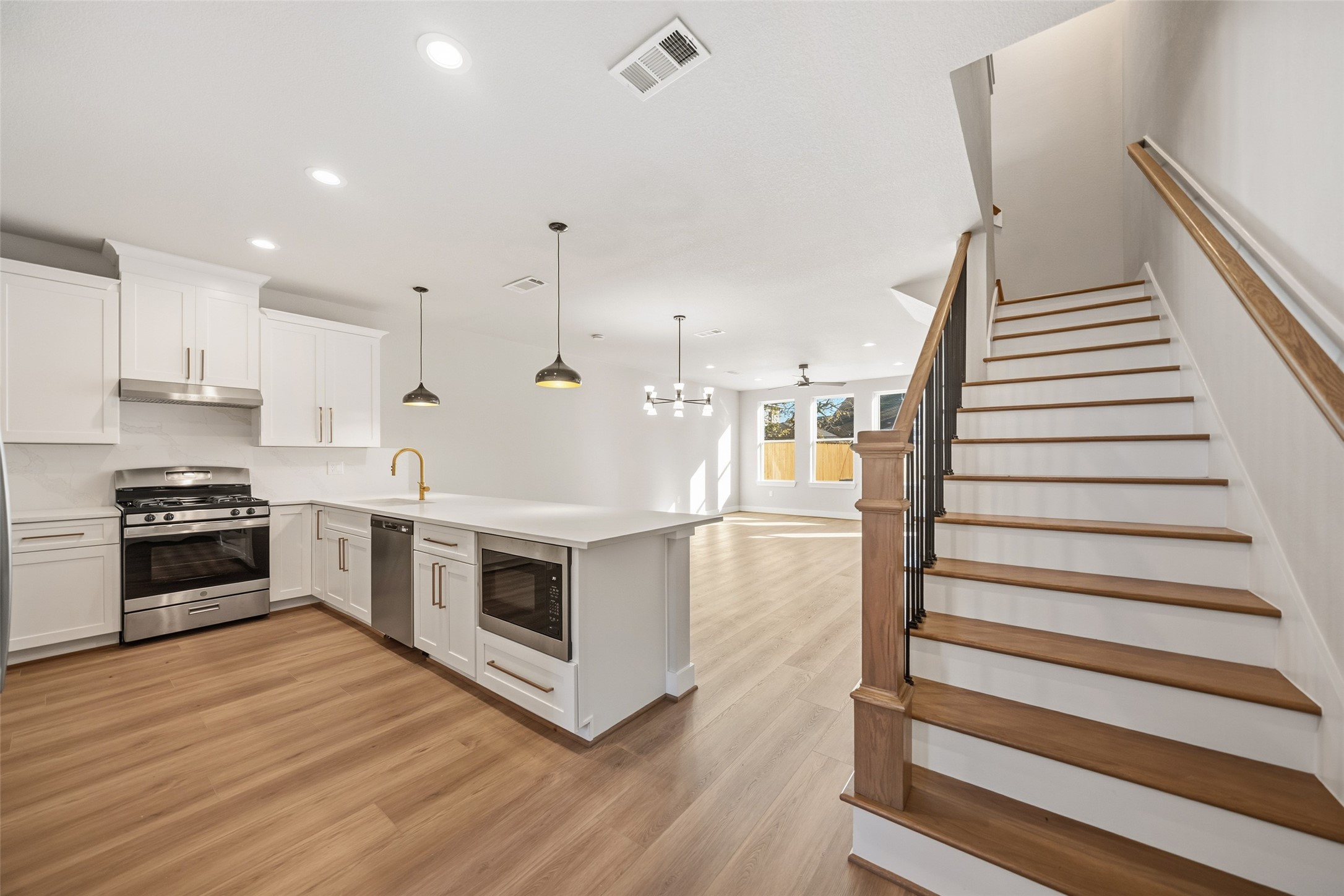 3422 Elser Street Houston, TX 77009 - Photo 9 of 26 This modern home features an open-concept layout with a spacious kitchen, complete with white cabinets, stainless steel appliances, and an island. The adjacent living area is bright with natural light and has wood flooring throughout. The staircase adds an elegant touch, leading to the upper level.