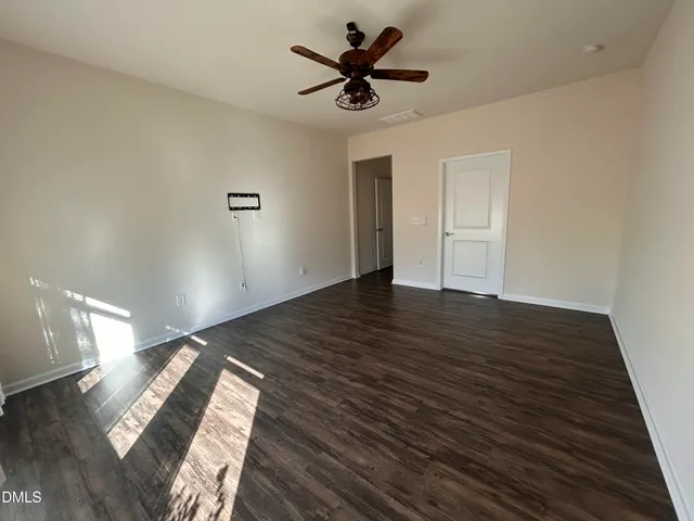 a view of an empty room with wooden floor and a ceiling fan