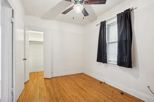 a view of an empty room with wooden floor and a ceiling fan