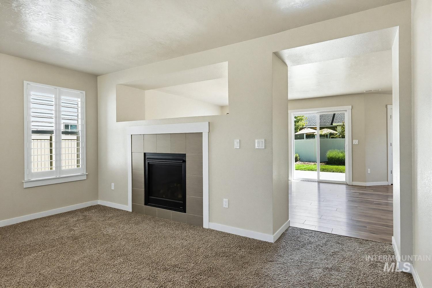 846 North Hidden View Way Star, ID 83669 - Photo 7 of 49 Living area featuring a tile-surround fireplace with a white mantel, plantation shutters, and carpet flooring