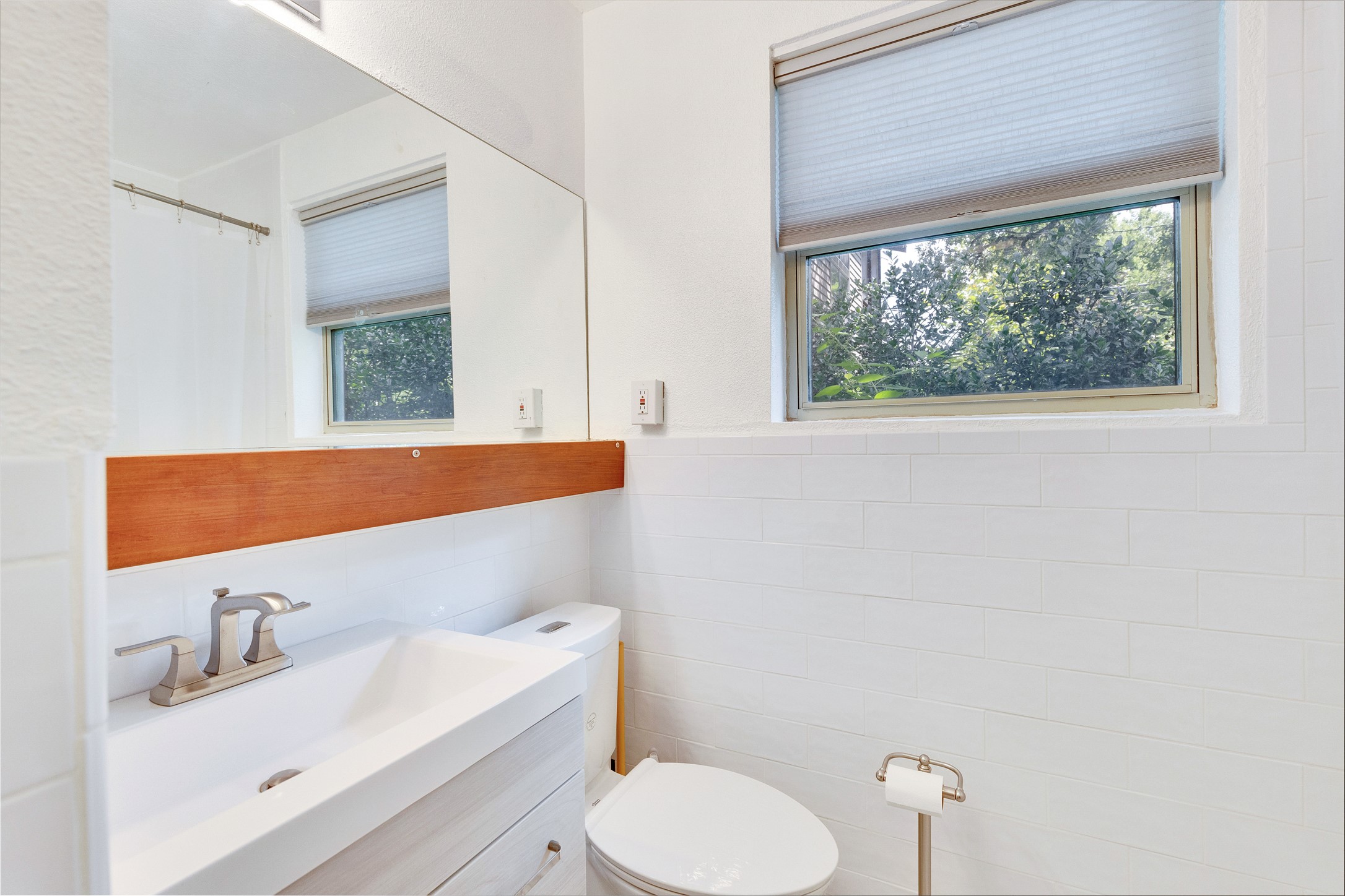 1306 Norwood Road, Unit A Austin, TX 78722 - Photo 17 of 21 A well-lit bathroom features white subway tile, a sleek vanity, and a window framing lush outdoor greenery.