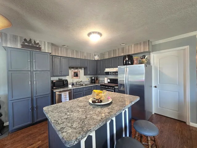 a kitchen with stainless steel appliances granite countertop a dining table chairs refrigerator and stove